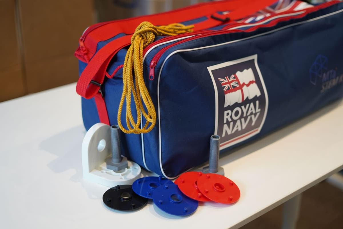 A blue and red Royal Navy bespoke MTa kit with a rope on top, alongside colorful circular plastic pieces and hardware components on a white table.