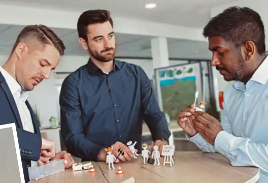 Group of men playing Playmobil Charades, using figurines to represent activities for others to guess.